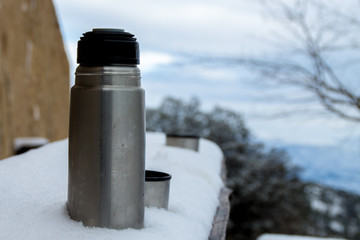 Aluminum thermos for tea or hot drinks, on snowy ground