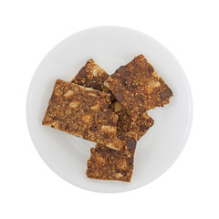 Top view of several broken almond butter chocolate nut bars on a plate isolated on a white background.