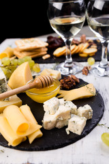 Cheese plate. Assortment of cheese with walnuts, bread an honey on stone slate plate.