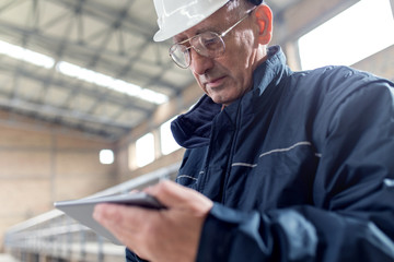 Senior construction manager controlling building site. He is holding tablet in his hands. 