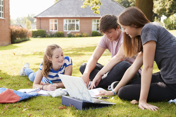 Teenage Students Sitting Outdoors And Working On Project