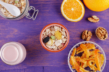 Healthy breakfast. Ceramic bowl with oat flakes, dried fruits, nuts on a violet wooden background