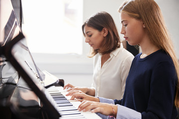 Female Pupil With Teacher Playing Piano In Music Lesson