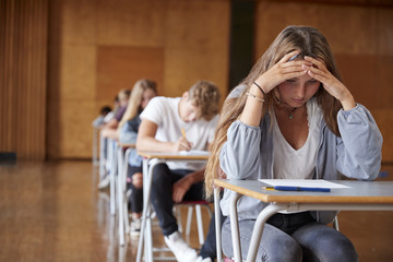 Anxious Teenage Student Sitting Examination In School Hall - obrazy, fototapety, plakaty
