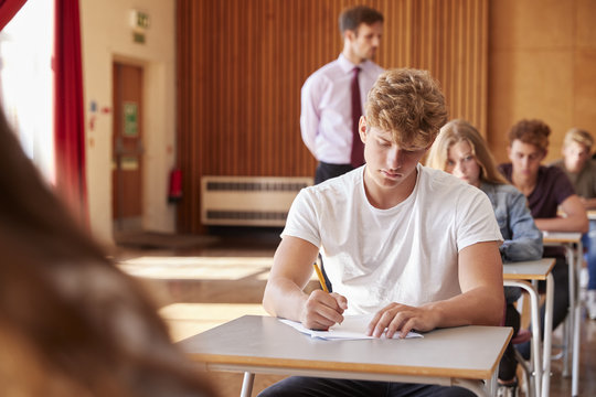 Teenage Students Sitting Examination With Teacher Invigilating