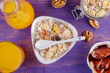 Healthy breakfast. Ceramic bowl with oat flakes, dried fruits, nuts on a violet wooden background
