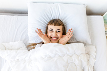 overhead view of happy woman looking at camera while resting in bed in morning