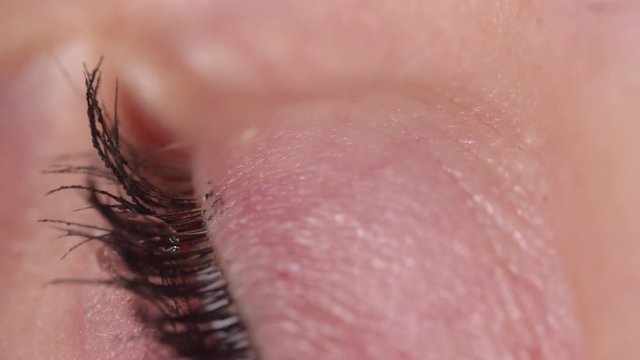 SLOW MOTION MACRO: Detailed view of water drop making contact with surface of brown eye. Mascara covered lashes flinch when droplet hits eyeball. Female applies eye drops to soothe eye discomfort.