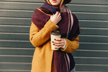 partial view of woman in autumn jacket and hat with coffee to go in hand