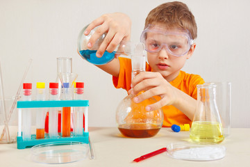 Little smart boy in safety goggles studies chemical practice in the laboratory