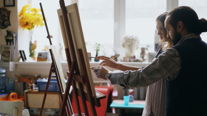 Skilled artist man teaching young girl to drawing paintings and explaining the basics in art studio
