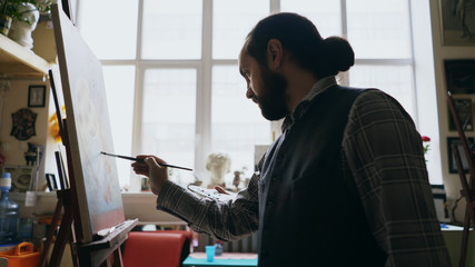 Skilled artist man teaching young woman painting on easel at art school studio - creativity, education and art people concept