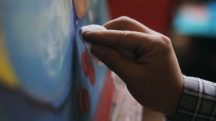Close-up of artist's hand smearing oil paints on canvas picture in art workshop