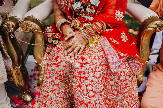 Stunning Indian bride dressed in Hindu traditional wedding clothes lehenga embroidered with gold and a veil during Saptapadi ceremony holds golden accessories on her knees