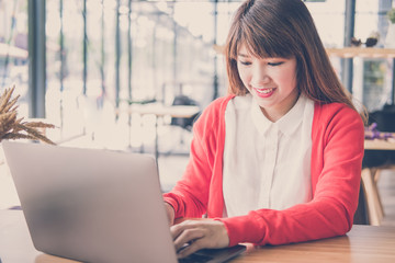 start up woman wearing red cardigan typing on computer at home. freelance female adult working with laptop at cafe. education, business concept.