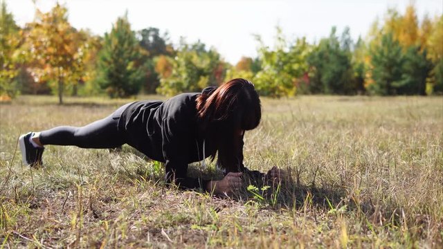 Woman having regular sport training. She working out in autumn park and doing plank exercise