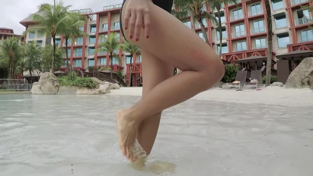 Video footage of unknown woman legs walking on the luxury hotel pool with white sand and wearing swimsuit