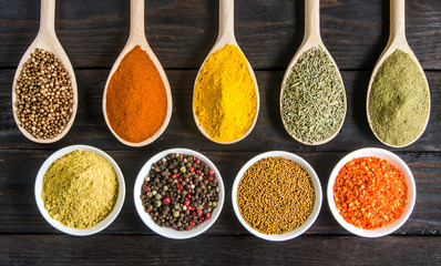 different spices in wooden spoons on a black wooden background
