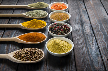 different spices in wooden spoons on a black wooden background