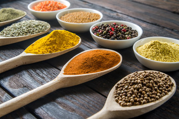 different spices in wooden spoons on a black wooden background