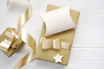 Mockup Christmas greeting card with gold gift ribbon, flatlay on a white wooden background, with place for your text