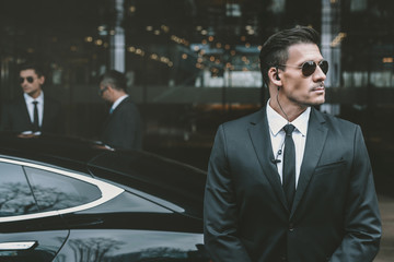 bodyguard standing at businessman car and reviewing territory - Powered by Adobe