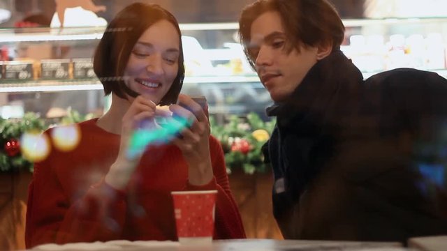 Young couple smiling using smartphone sitting in cafe. Christmas time