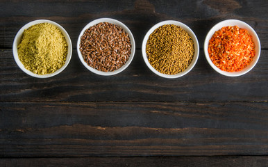 different spices in wooden spoons on a black wooden background