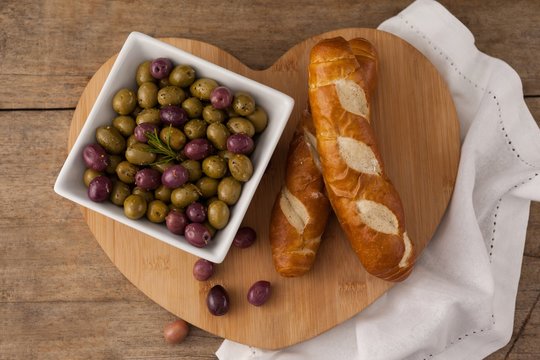 Overhead view of olives and bread on heart shape cutting board