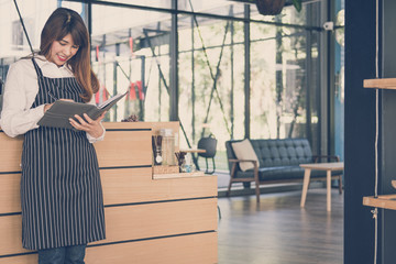 small business owner holding notebook at counter in coffee shop. female barista wearing apron writing note at bar in cafe. food service, restaurant concept.