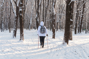 Nordic walking. Woman in a white jacket with a backpack hiking in a cold snow forest. Scenic...