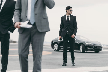cropped image of bodyguards and businessman walking on helipad from car