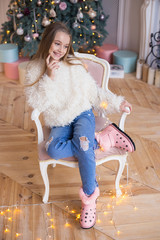 Little happy girl sits on a background of Christmas decorations in stylish and fashionable clothes