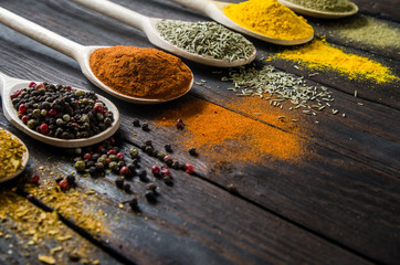 different spices in wooden spoons on a black wooden background © gerik_a