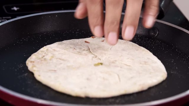 Flipping paratha on a hot pan, while pouring oil on it. - Close up