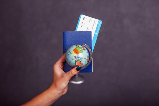Womans hand holding international passport, airplane ticket and globe before grey isolated background