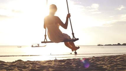 Slow motion footage of happy woman on rope swing at the beach during vacation holidays and crossing the sun, travel destination leisure concept