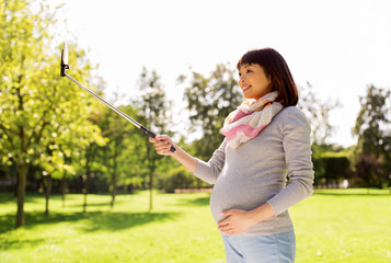 happy pregnant asian woman taking selfie at park