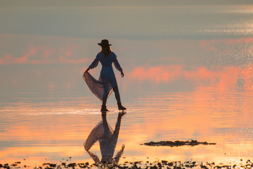 Young girl in dress and black hat walking on the salt lake beach