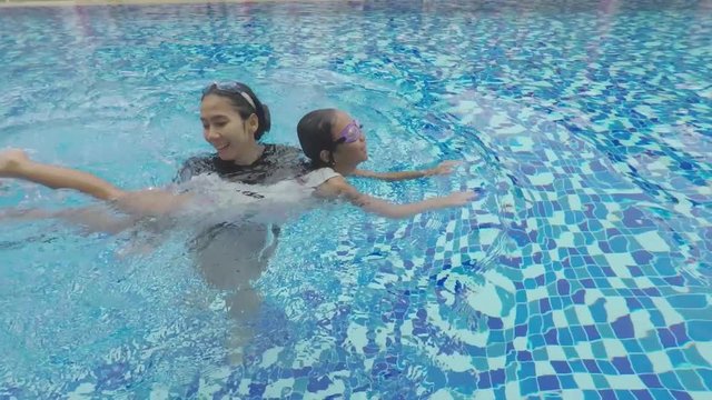 Video footage of a young Asian mother teaching her daughter to swim on the pool while wearing swimsuit