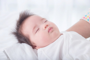 Fototapeta na wymiar Little asian baby girl wearing white cloth sleeping on her mother arm