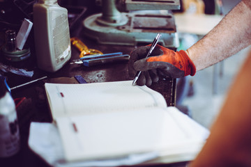 Senior man in workshop. Man writing obligations in his notes. Close up.
