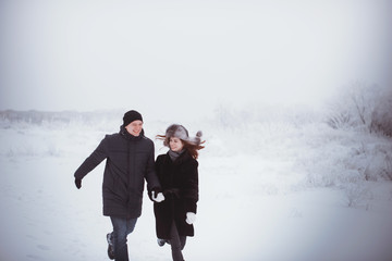 A loving couple on a winter walk. Snow love story, winter magic. Man and woman on the frosty street. The guy and the girl are resting on the snow. Christmas mood of a young family.