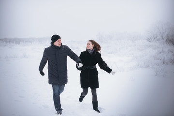 A loving couple on a winter walk. Snow love story, winter magic. Man and woman on the frosty street. The guy and the girl are resting on the snow. Christmas mood of a young family.