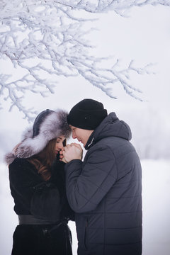 A loving couple on a winter walk. Snow love story, winter magic. Man and woman on the frosty street. The guy and the girl are resting on the snow. Christmas mood of a young family.