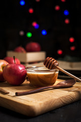 cooking of baked apples for New Year's holidays, Christmas tree and New Year's lights, honey and cinnamon on a wooden cutting board on a dark background