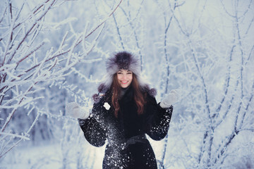 Beautiful happy laughing young woman wearing winter hat gloves  covered with snow flakes. Winter forest landscape background