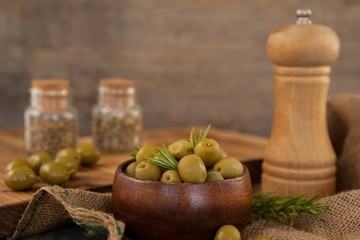 Olives and rosemary in bowl by pepper shaker
