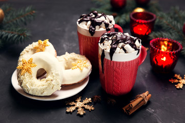 Christmas hot cacao in red cups with marshmellows and chocolate donuts festive background with candles