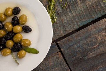 Overhead view of green and dry black olives with oil in plate